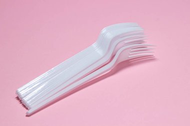 Pembe arka planda plastik çatallar. Tek kullanımlık sofra takımı. Plastik ürünler.