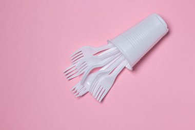 Pembe arka planda plastik tabaklar. Plastik bardaktaki plastik çatallar. Tek kullanımlık sofra takımı. Plastik ürünler.