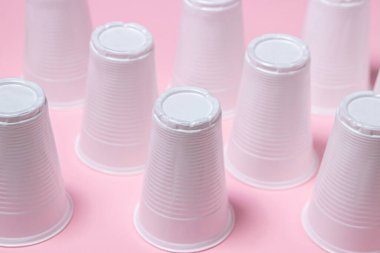 Pembe arka planda plastik gözlük. Tek kullanımlık sofra takımı. Plastik ürünler.