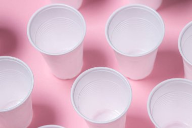 Pembe arka planda plastik gözlük. Tek kullanımlık sofra takımı. Plastik ürünler.