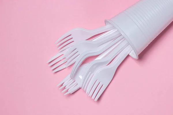 Plastic dishes on a pink background. Plastic forks in a plastic cup. Disposable tableware. Plastic products.