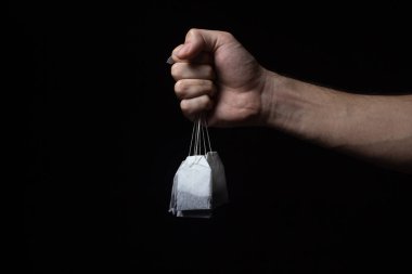 Bir el siyah arka planda birkaç çay poşeti tutar. Koyu arkaplanda çay poşetleri