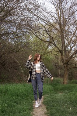 Kız doğada yol boyunca yürür. Ormanda bahar yürüyüşü. Doğanın arka planında genç bir kız