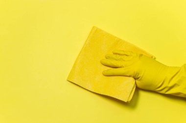 Sarı arka planda temizlik aletleri. Eldivenli bir el bezi ile siliyor. Ev yıkama ve temizlik aletleri.