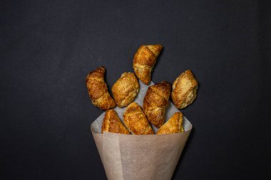 Siyah bir yüzeyde kruvasanlar. Koyu bir arka planda pişirme. Kağıt zarfın içinde tatlı hamur işleri