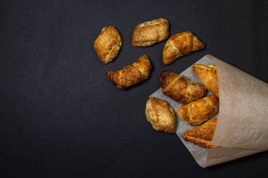 Siyah bir yüzeyde kruvasanlar. Koyu bir arka planda pişirme. Kağıt zarfın içinde tatlı hamur işleri