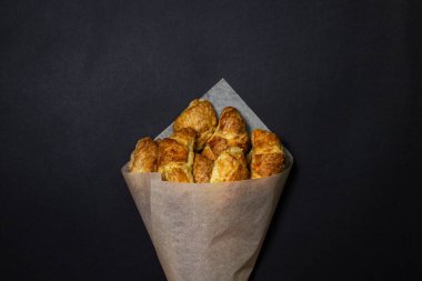 Siyah bir yüzeyde kruvasanlar. Koyu bir arka planda pişirme. Kağıt zarfın içinde tatlı hamur işleri