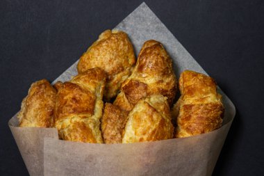 Siyah bir yüzeyde kruvasanlar. Koyu bir arka planda pişirme. Kağıt zarfın içinde tatlı hamur işleri