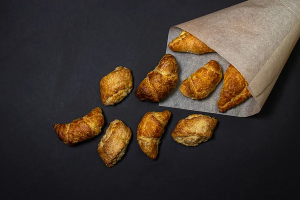Siyah bir yüzeyde kruvasanlar. Koyu bir arka planda pişirme. Kağıt zarfın içinde tatlı hamur işleri