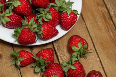 Ahşap bir masada bir tabakta çilek. Olgun taze çilekler. Sağlıklı beslenme.