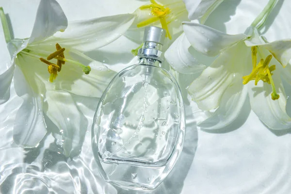 Perfume bottle and white flowers on the water surface. Circle ripples on water surface. Pure clear water