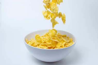 Mısır gevrekleri beyaz arka planda bir tabağa düşer. Sağlıklı ve lezzetli bir kahvaltı..