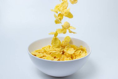 Mısır gevrekleri beyaz arka planda bir tabağa düşer. Sağlıklı ve lezzetli bir kahvaltı..