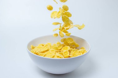 Mısır gevrekleri beyaz arka planda bir tabağa düşer. Sağlıklı ve lezzetli bir kahvaltı..