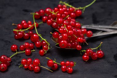 Siyah arka planda çay kaşığı kırmızı frenk üzümü. Bir sürü olgun kırmızı frenk üzümü. Lezzetli meyve.