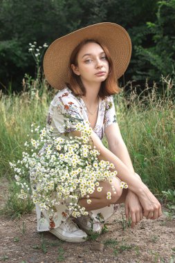 Güzel bir kız doğada elinde bir buket papatya tutuyor. Doğanın tadını çıkaran çiçekli bir kızın nazik portresi..