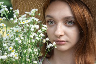 Güzel bir kız doğada elinde bir buket papatya tutuyor. Doğanın tadını çıkaran çiçekli bir kızın nazik portresi..