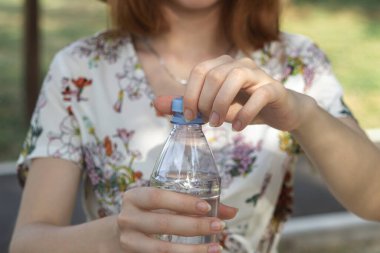 Kız bir şişe su açıyor. Plastik şişedeki saf içme suyu. Su şişesini açıyorum.
