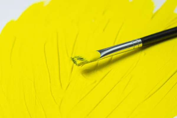 Brush for painting with yellow paint on a yellow background. Watercolor paint