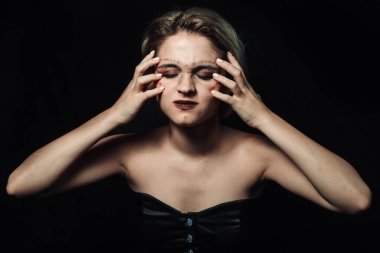 Siyah arka planda bir kadın. Makyajlı bir kız. Elleri acı içinde başını tutan bir kız.