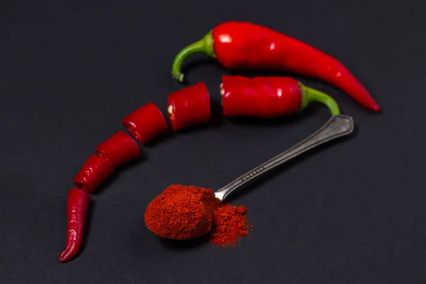 Red ground pepper next to a whole red hot pepper on a black background. Chili pepper isolated