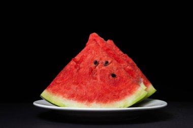 Siyah arka planda beyaz bir tabakta dilimlenmiş karpuz. Sulu karpuz dilimleri