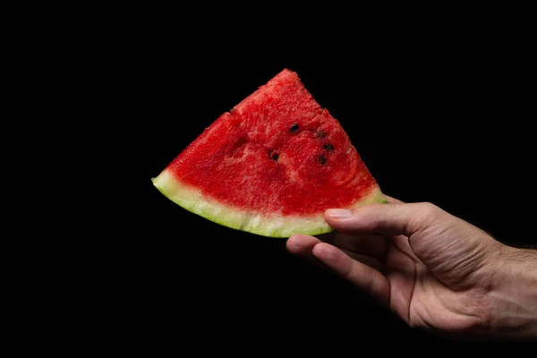 Hand holds a slice of watermelon on a black background. Slices of juicy watermelon