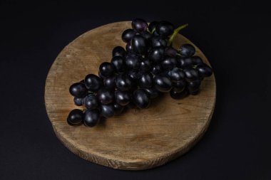 Siyah arka planda siyah üzümler. Koyu bir arka planda tahta üzerinde bir demet üzüm.