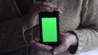 Kadın elleri cep telefonunu yeşil ekranla yukarıda tutuyor. 