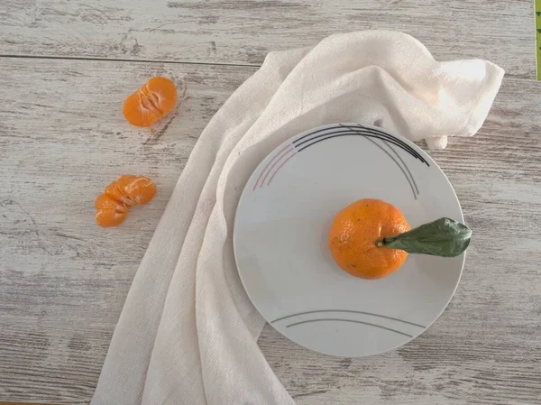 Mandalina meyvesi beyaz masa arkasında plaka olan kumaş bir kumaşın üzerinde yatıyor.