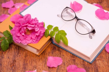 Açık bir kitap, okunacak bardaklar ve ahşap bir masada gül çiçeği yaprakları.