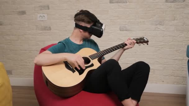 Młody człowiek siedzi na woreczku z okularami VR gra na gitarze. — Wideo stockowe
