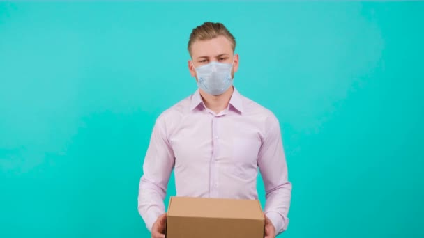 Egy férfi maszkot visel, miközben egy dobozt tart, és a stúdióban áll.. — Stock videók