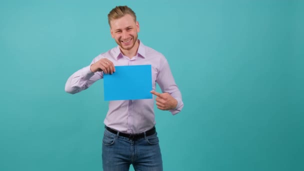 Ένας γενειοφόρος χαρούμενος νεαρός δείχνει ένα μπλε σεντόνι που κρατάει στο χέρι του.. — Αρχείο Βίντεο