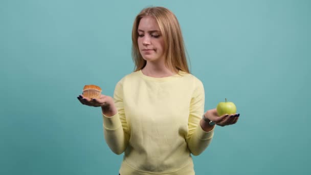 Młoda kobieta wybierając między jabłkiem i babeczką, dziewczyna jest wybrać babeczkę. — Wideo stockowe