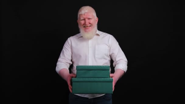 Hombre albino guapo que da una caja de regalo desde el corazón, mirando a la cámara. — Vídeo de stock