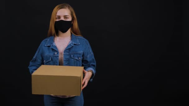 Egy nő maszkot visel, miközben egy csomagot tart, és a stúdióban áll.. — Stock videók