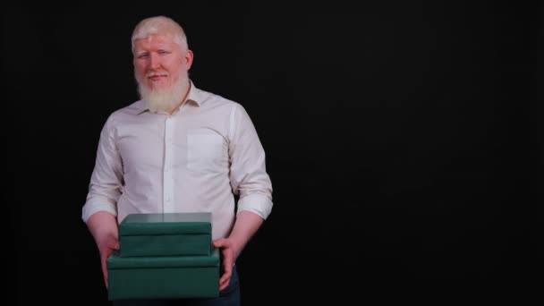 Bonito albino homem que dá uma caixa de presente, olhando para a câmera com um sorriso. — Vídeo de Stock