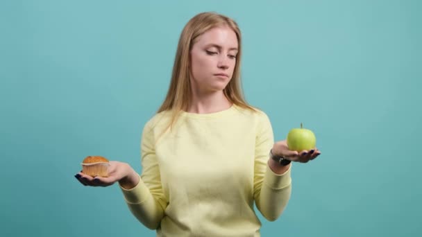Νεαρή γυναίκα διαλέγει ανάμεσα σε μήλο και κεκάκι, το κορίτσι διαλέγει μήλο.. — Αρχείο Βίντεο