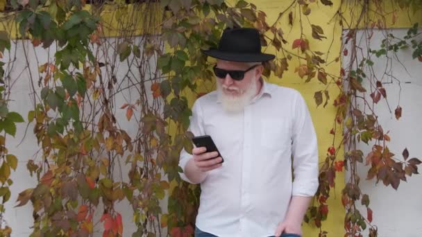Velho com albinismo surfando na internet enquanto sentado ao lado de sua casa. — Vídeo de Stock