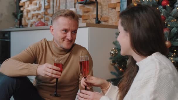 Genç çift Noel ağacının yanında oturup öpüşürken şampanya içiyor.. — Stok video
