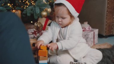 Bir kız çocuğu Noel ağacının yanında oturmuş babasıyla oynuyor..