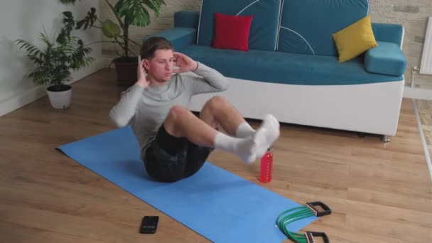 Молодий чоловік робить вправи на животі вдома на синьому килимку . — стокове відео