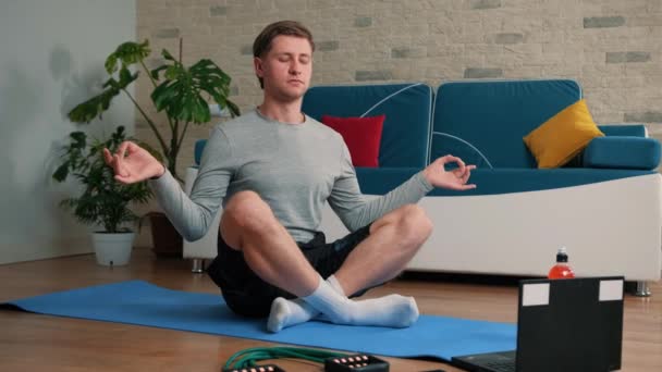 Jeune homme méditant dans la pose de lotus sur le tapis d'exercice à la maison. — Video