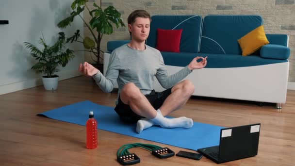 Jeune homme méditant dans la pose de lotus sur le tapis d'exercice à la maison. — Video