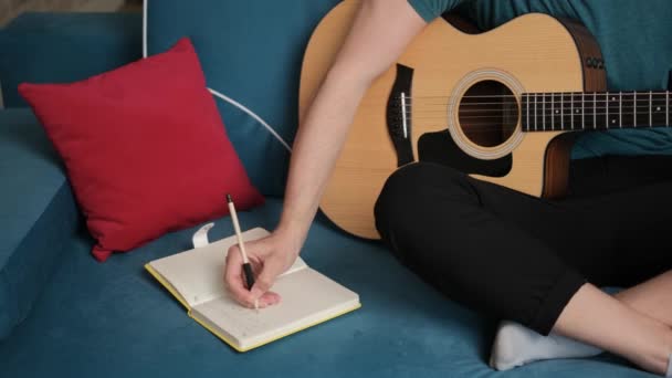 Gros plan d'une main de guitariste qui écrit une nouvelle idée de chanson dans un carnet. — Video