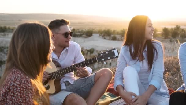 Jeune homme joue de la guitare tout en se reposant avec ses amis au pique-nique d'été. — Video