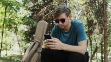 Genç adam arkadaşlarıyla sohbet ederken parkta bankta oturuyor..