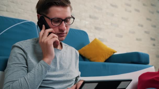 Man aan de telefoon praten terwijl hij werkt aan laptop, zittend op boonzak thuis. — Stockvideo