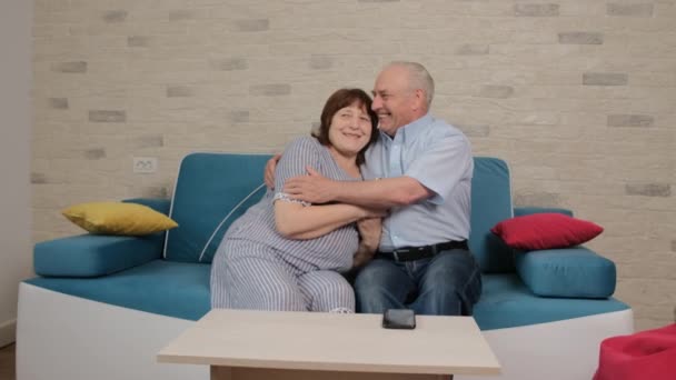 Seniorenpaar sitzt auf Sofa und erzählt von glücklichen Momenten zusammen.
